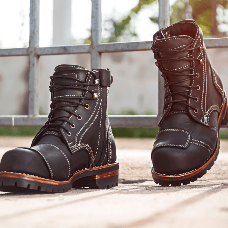 Rugged men's boots, including ankle, work, and hiking boots, displayed on a textured outdoor surface with strong lighting.