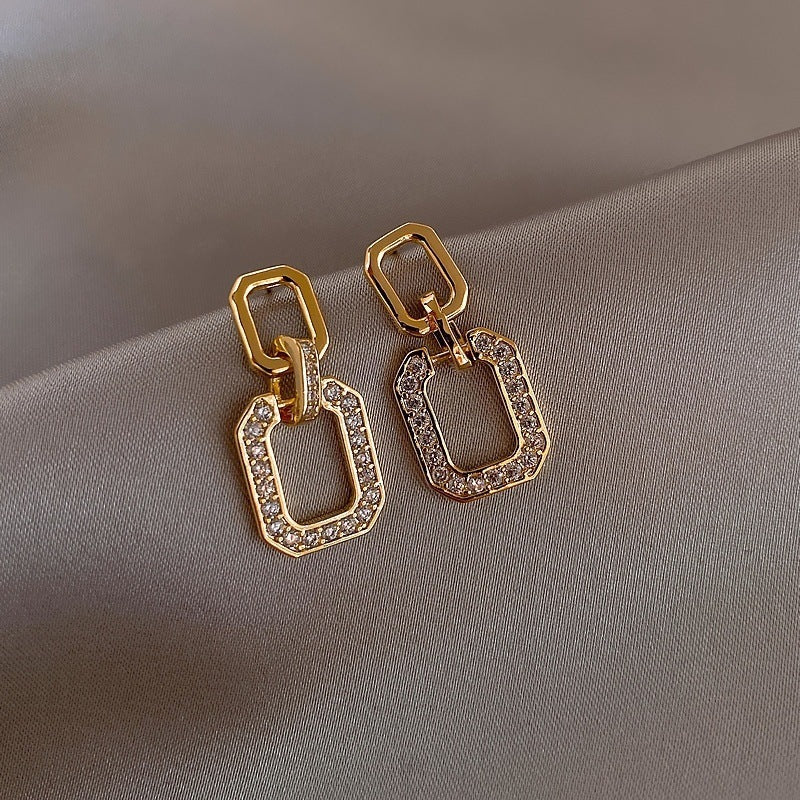 Geometric gold drop earrings with pavé edges on satin background