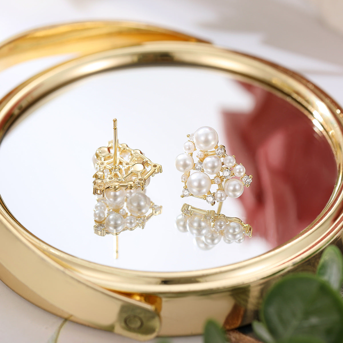 Pair of pearl earrings on a gold compact mirror with a blurred background
