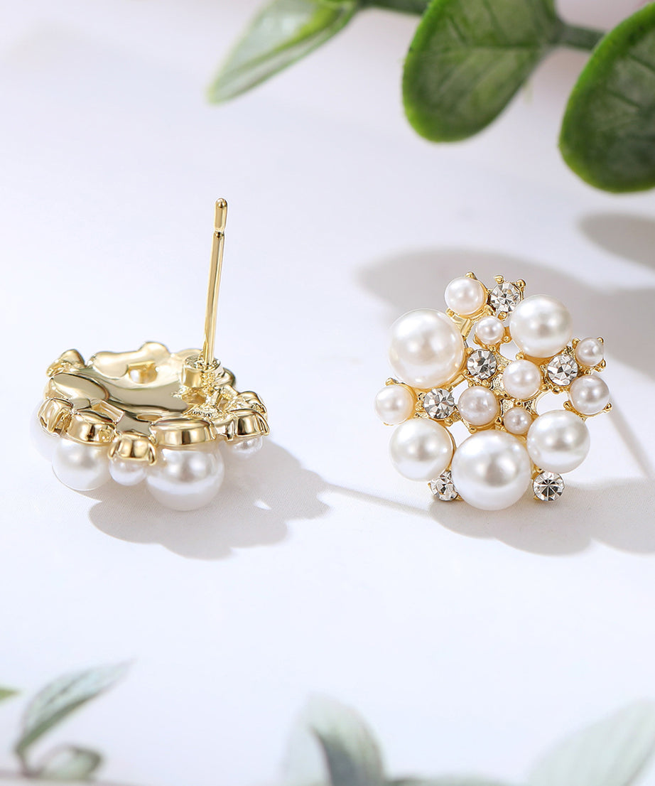 Pearl and gold earrings on a light background with green leaves.