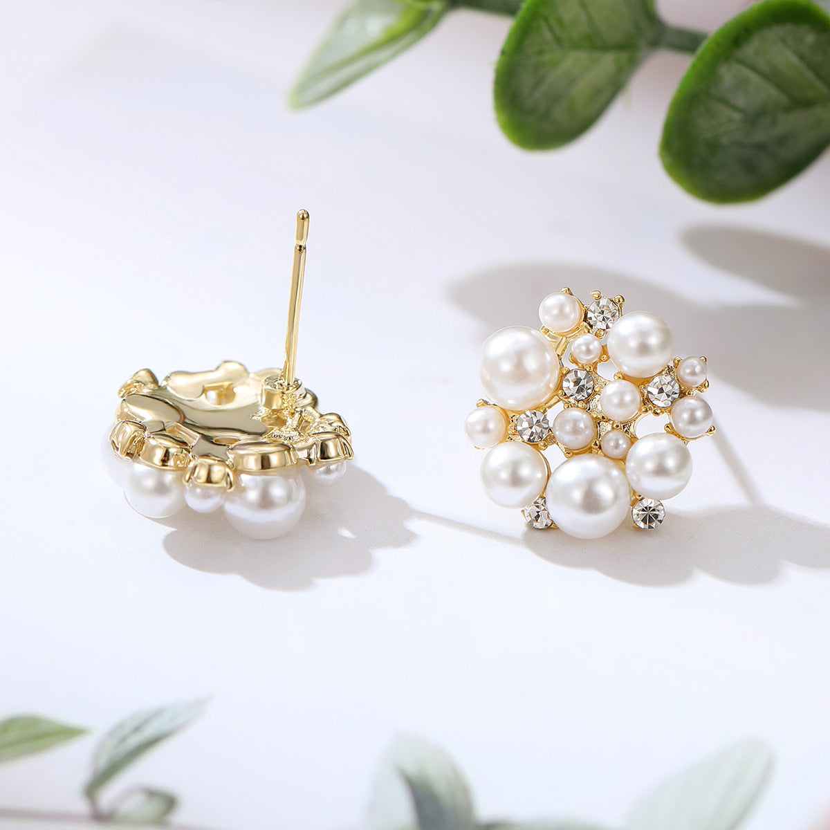 Pearl and gold earrings on a light background with green leaves.