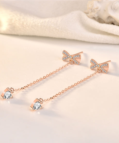 Rose-gold bow tassel stud earrings on fabric background