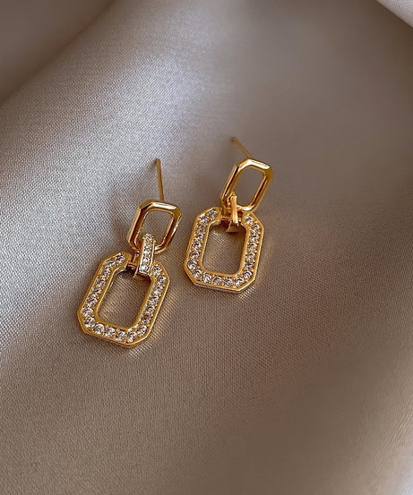 Gold earrings with diamond accents on a beige fabric background